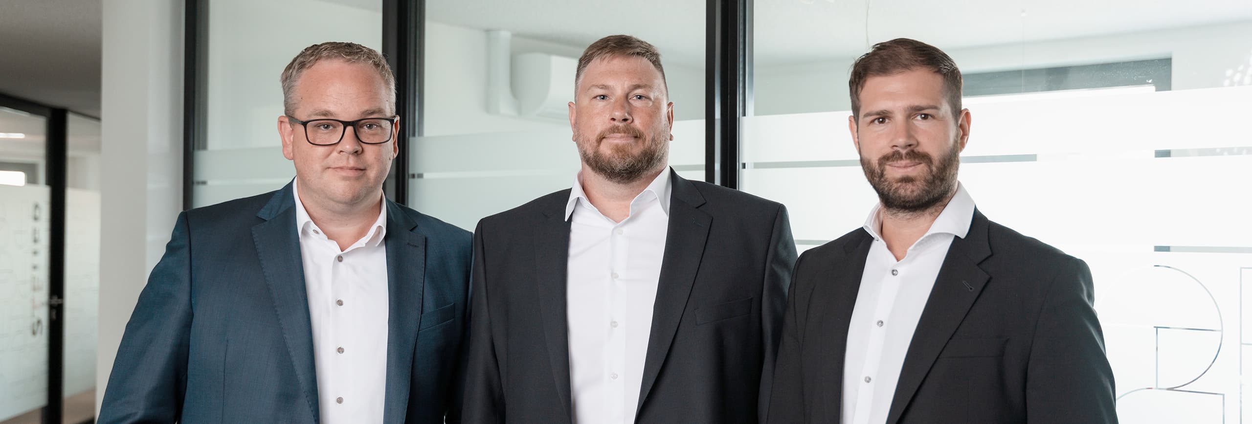 Die drei Geschäftsführer von J2B stehen nebeneinander vor einer Glasfront